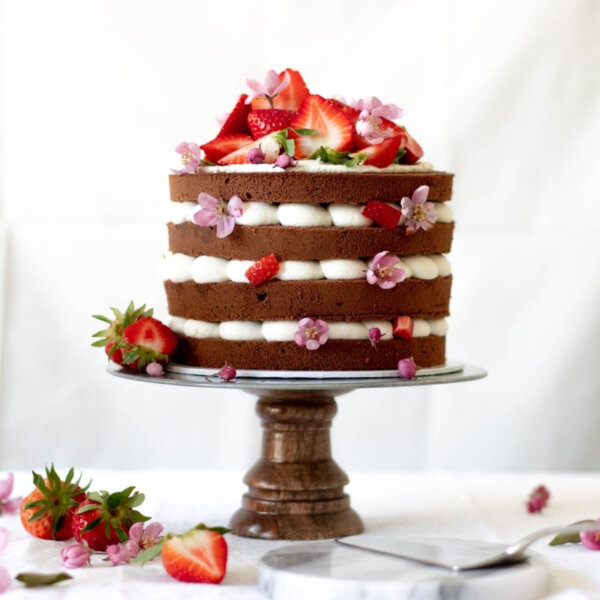 A strawberry cake with four cocoa bases and cream in between on a cake stand