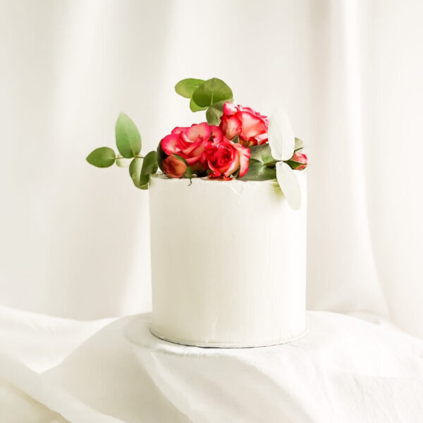 Eine einstöckige Geburtstagstorte mit glattem Cremeinstrich in weiß und rosa Rosen oben auf.