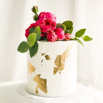 Eine einstöckige Torte mit Blattgold an der Seite und Blumen.