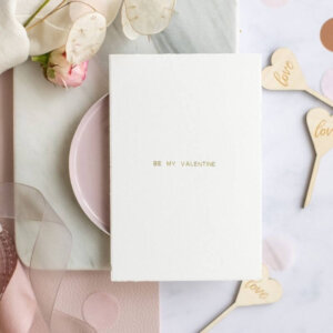 A white greeting card with a golden inscription be my valentine
