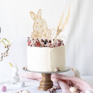 A small one tier cream cake with cherry blossoms on a cake stand and Happy Easter cake topper