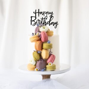 A cake with many colorful macarons on the side and a caketopper Happy Birthday