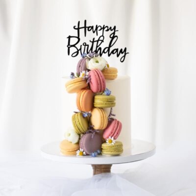 Eine Torte mit vielen bunten Macarons an der Seite und einem Caketopper Happy Birthday