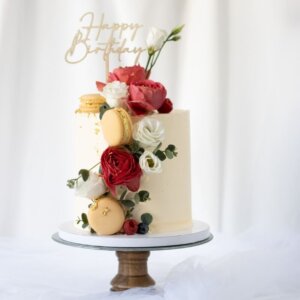Single tier cake on etagere. Decorated with flowers, macarons and gold leaf, caketopper.