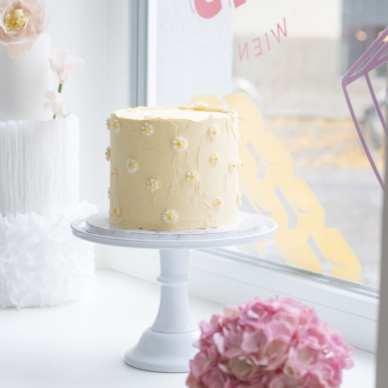 Eine einstöckige Torte in zartem gelb mit strukturierter Oberfläche und handmodellierten Gänseblümchen